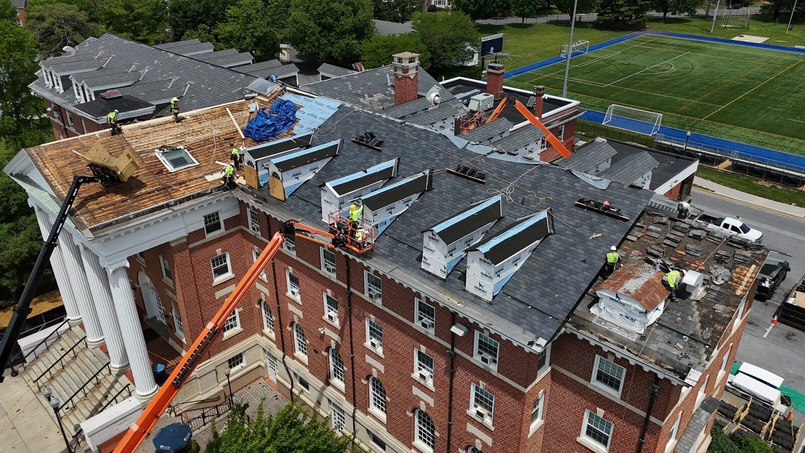Crews re-roofing a historic brick institutional building with boom lifts