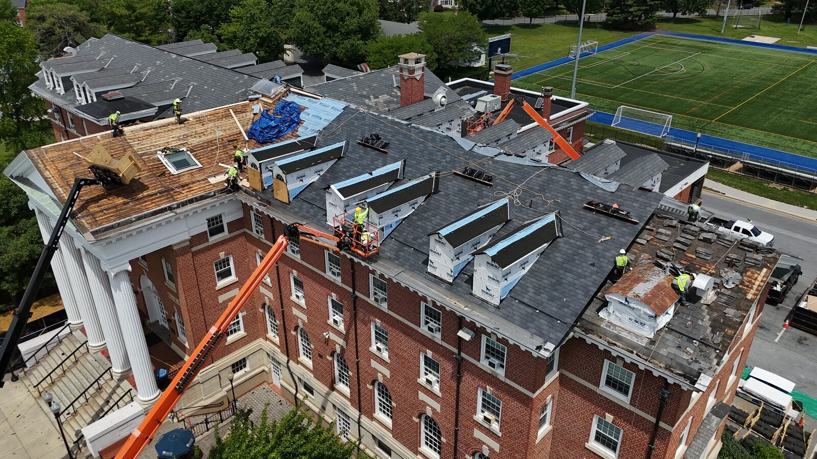 Crews re-roofing a historic brick institutional building with boom lifts