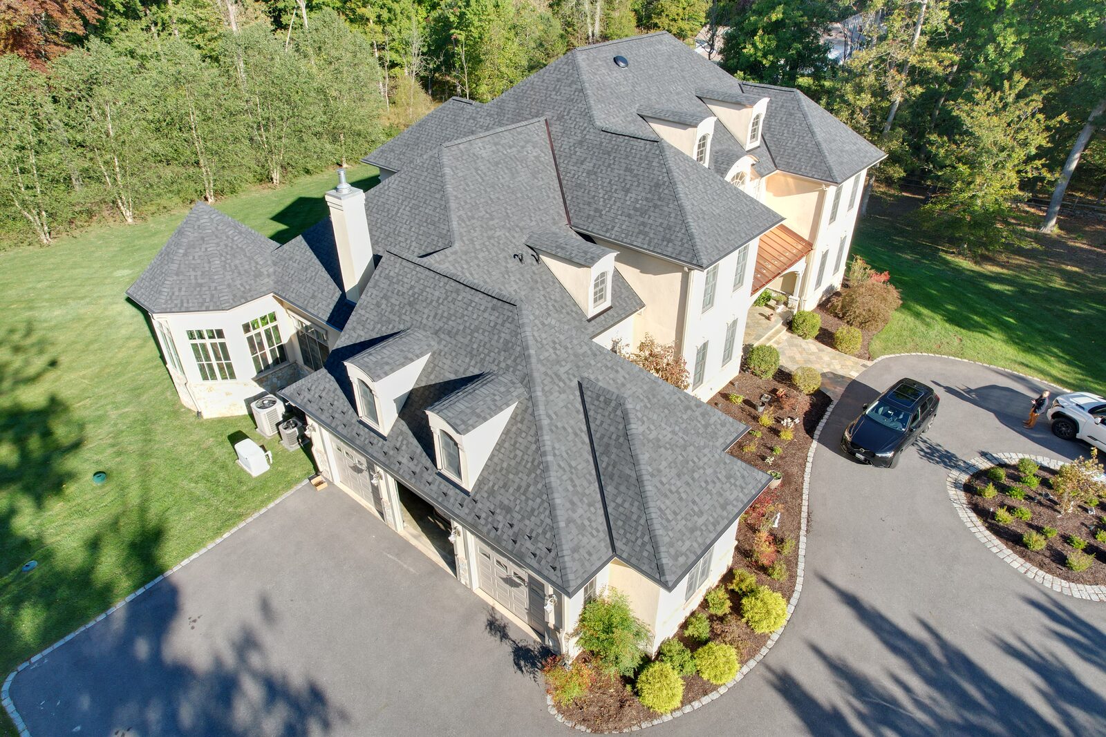 Aerial view of a stucco estate with a designer asphalt roof, turret, and dormers