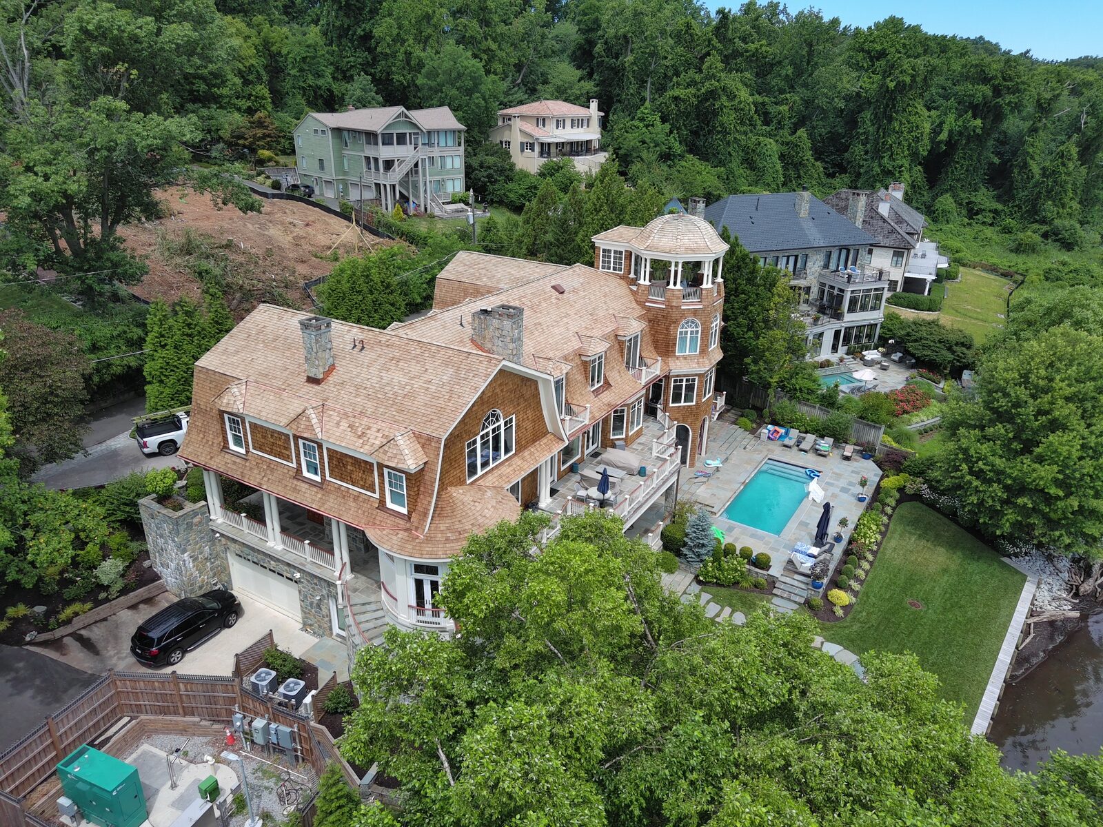 Aerial view of a shingle-style cedar estate with a turret and pool above the water